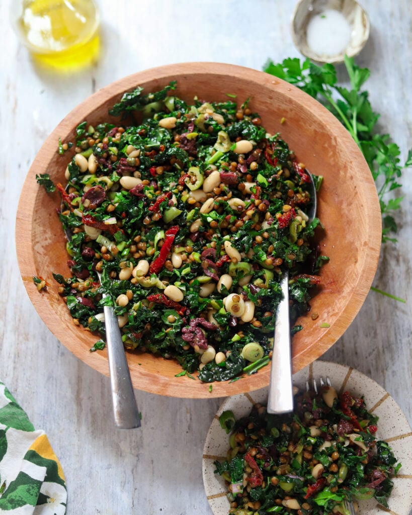 overhead view of a kale salad with lentils, beans, olives and sun-dried tomatoes in a wood bowl