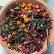 close up view into colorful beet and kale salad in a wooden bowl with a serving utensil