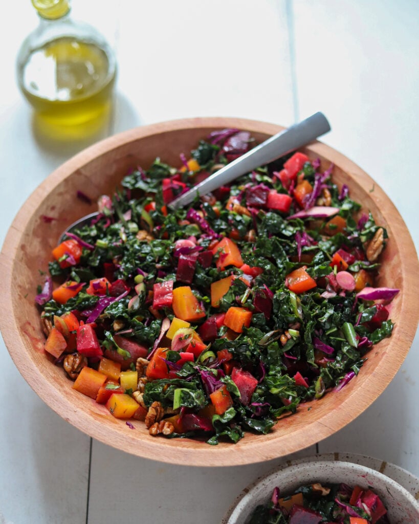 overhead at an angle view into colorful beet and kale salad in a wooden bowl with a serving utensil