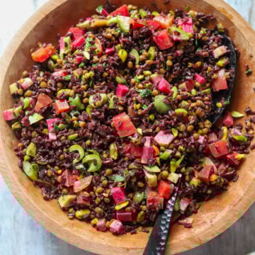 Big wooden bowl full of a colorful salad of rice, lentils and vegetables with a metal serving spoon