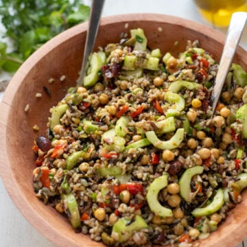 angled view of Mediterranean Wild Rice Salad with Chickpeas and Olives in a wood bowl with serving spoons