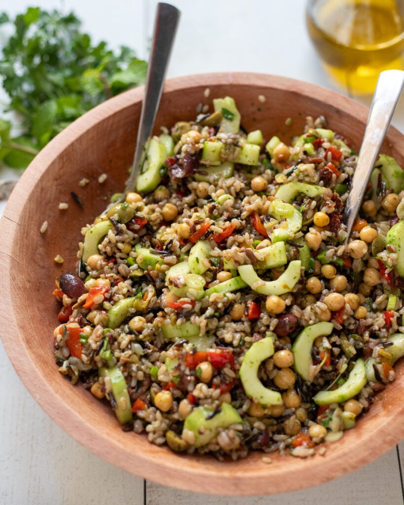 angled view of Mediterranean Wild Rice Salad with Chickpeas and Olives in a wood bowl with serving spoons