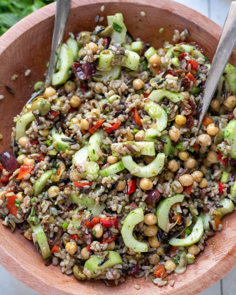close up view of Mediterranean Wild Rice Salad with Chickpeas and Olives in a wood bowl with serving spoons