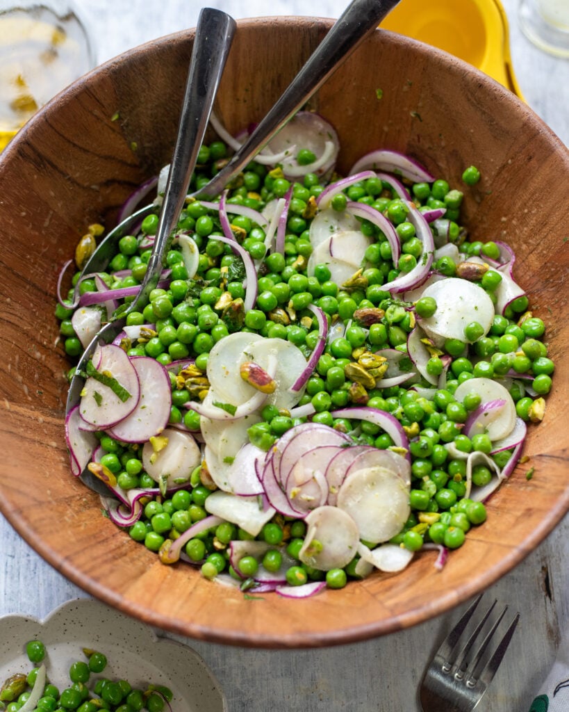 big wood bowl filled with healthy pea salad with radishes, red onions, mint and pistachios