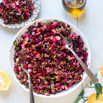 overhead view of large bowl of chimichurri lentil and beet salad with a jug of extra virgin olive oil , half a lemon and a small plate of salad surrounding the large bowl