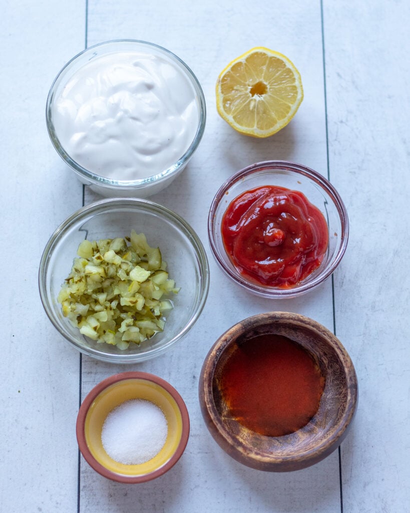 dressing ingredients laid outing small bowls: vegan yogurt, chopped pickles, salt, lemon, ketchup and hot sauce