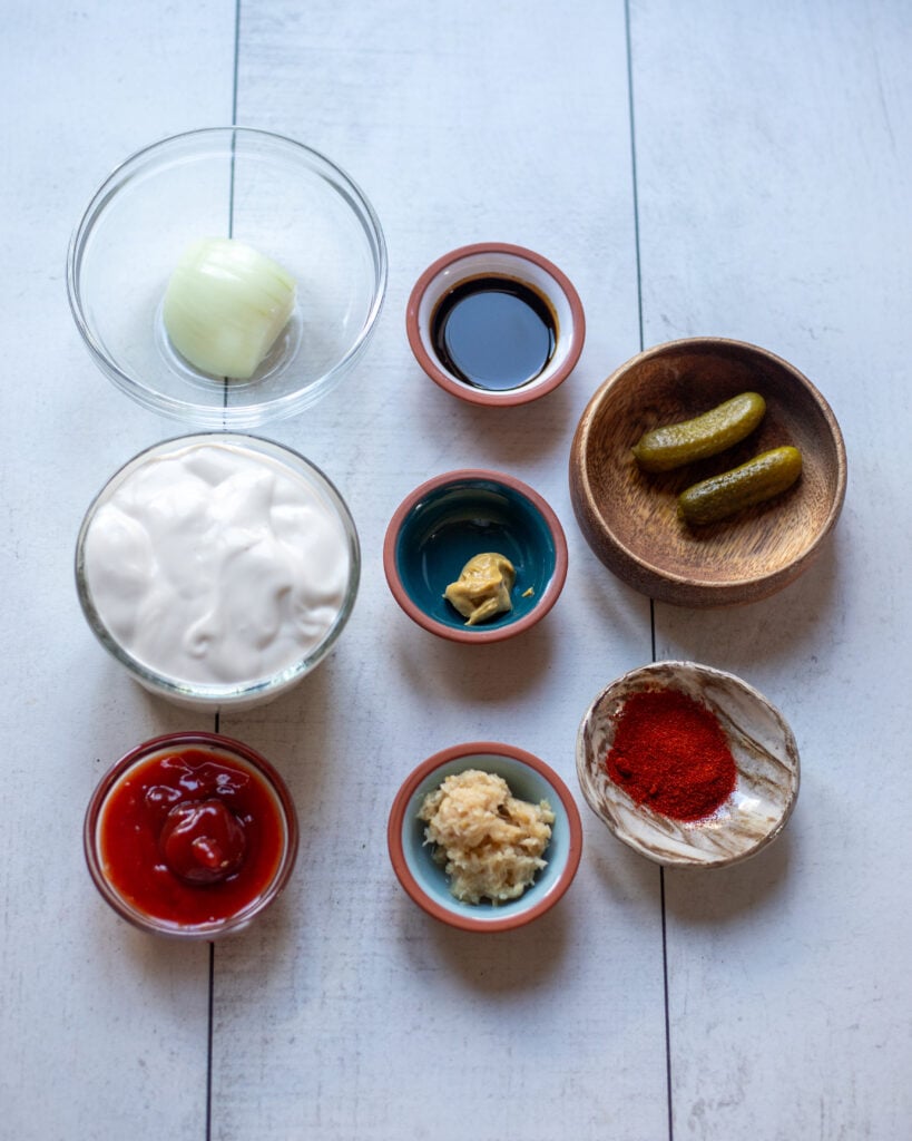 Ingredients in small bowls laid out in a tabletop: yogurt, onion, ketchup, mustard, horseradish, mustard, vegan Worcestershire, smoked paprika and pickles