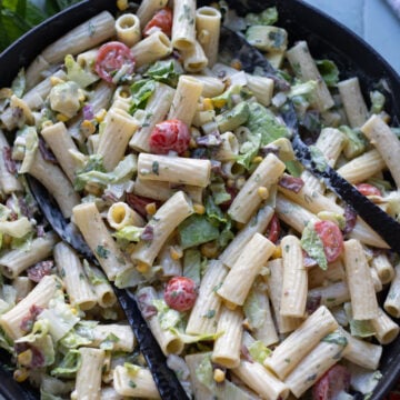 closeup of pasta salad in a black bowl with cherry tomatoes, corn, avocado and vegan bacon