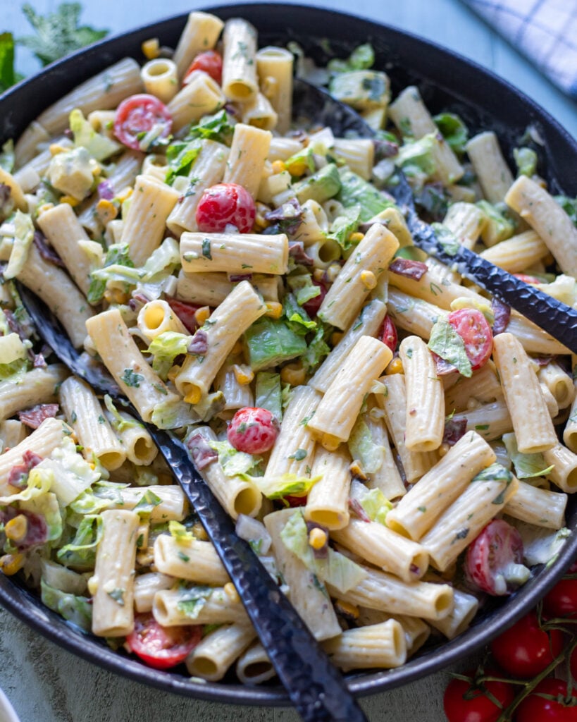 closeup of pasta salad in a black bowl with cherry tomatoes, corn, avocado and vegan bacon