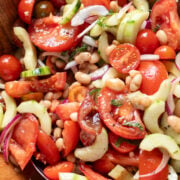 closeup view of a big wood bowl filled with a summer tomato salad with cucumbers, herbs, onions and beans