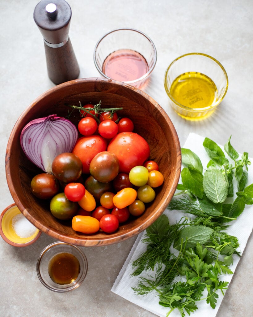 Ingredients for tomato and onion salad laid in a flat lay, tomatoes, onion, herbs, oil and vinegar, salt, pepper and maple syrup
