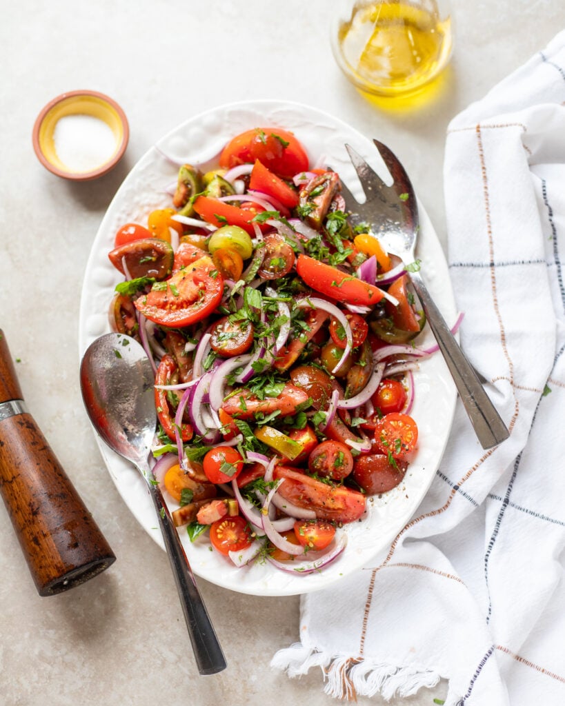 Overhead view of a platter of tomato and onion salad with herbs and vinaigrette