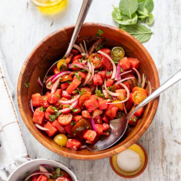 wide view of a wooden bowl filled with watermelon and tomato salad with fresh herbs and onions
