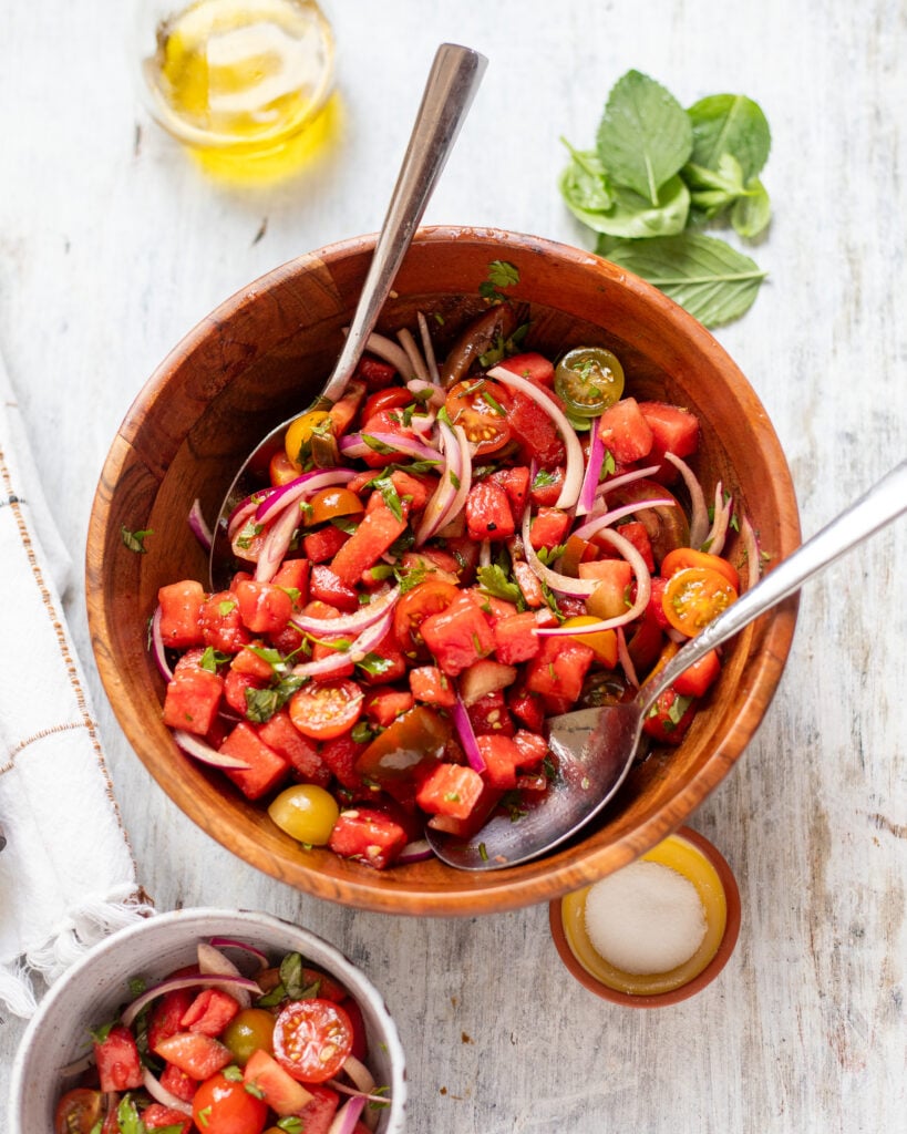 wide view of a wooden bowl filled with watermelon and tomato salad with fresh herbs and onions