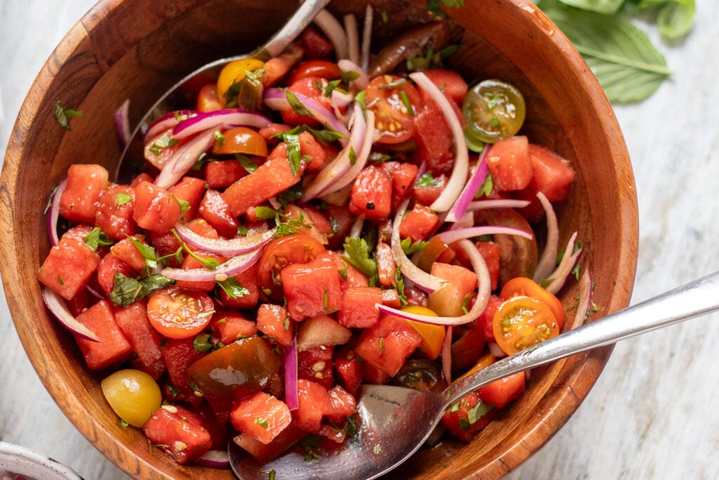 close up in a wood bowl filled with watermelon, tomato, herb and onion salad