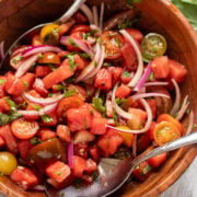 close up in a wood bowl filled with watermelon, tomato, herb and onion salad