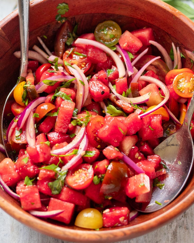 close up in a wood bowl filled with watermelon, tomato, herb and onion salad